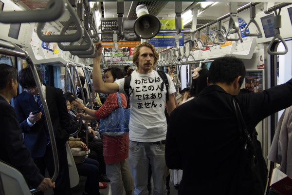 I took to the streets to sell my T-shirts. A white t-shirt with printed on it the text ‘I am not from here’.

私は自分でつくったTシャツを売るために街に出た。白いTシャツには「わたしはここの人ではありません。」という言葉がプリントされている。